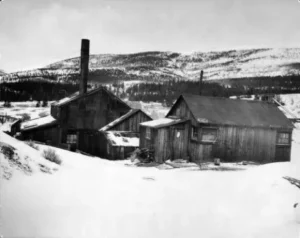 Historic image of the Matchless Mine’s superintendents’ cabin, hoist house, and headframe.
