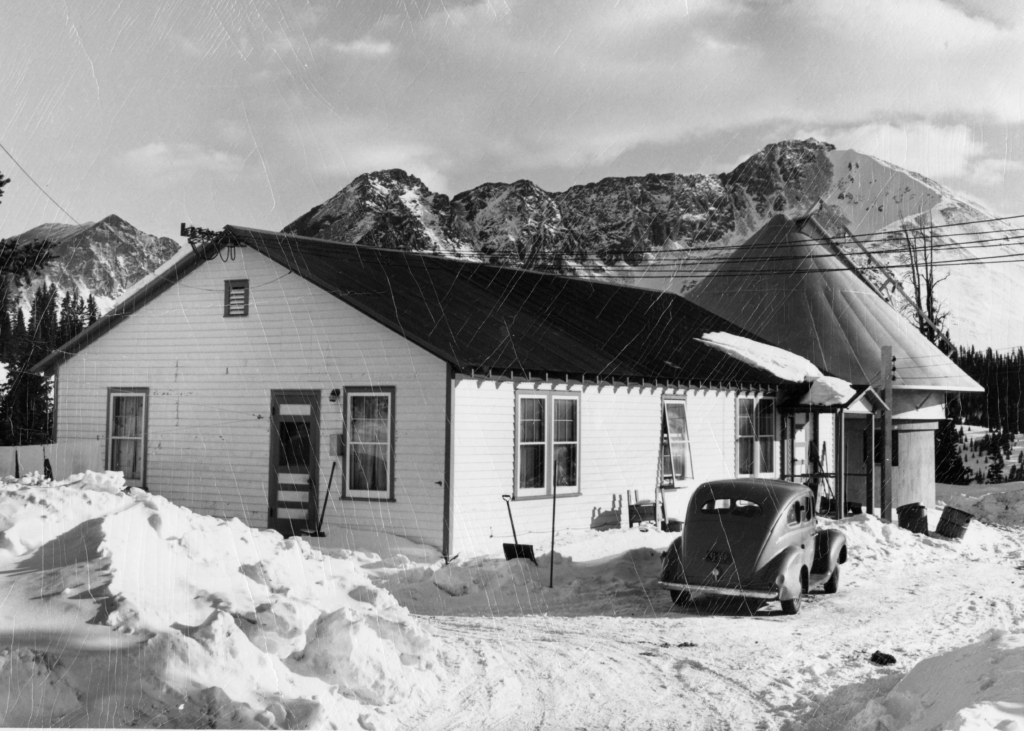 NSF NCAR Archives black and white image of a building with a car and snow in front of it. Mountains are in the background